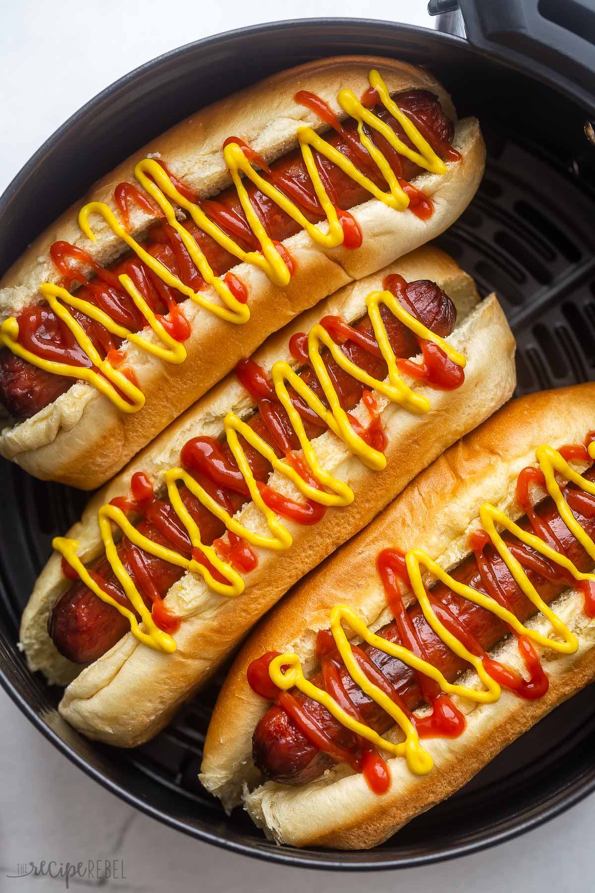 close up image of air fryer hot dogs in air fryer basket with ketchup and mustard