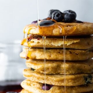 A stack of blueberry pancakes topped with fresh blueberries and maple syrup.