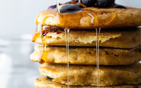 A stack of blueberry pancakes topped with fresh blueberries and maple syrup.