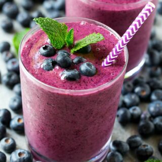 Blueberry smoothie served in a tall glass garnished with mint and fresh berries, with a striped straw.