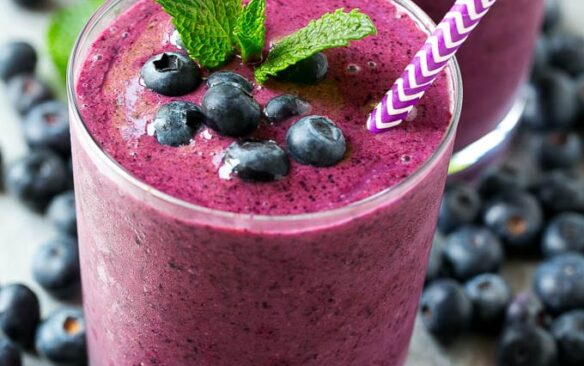 Blueberry smoothie served in a tall glass garnished with mint and fresh berries, with a striped straw.