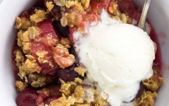 Top view of a bowl of cherry rhubarb crisp topped with ice cream.