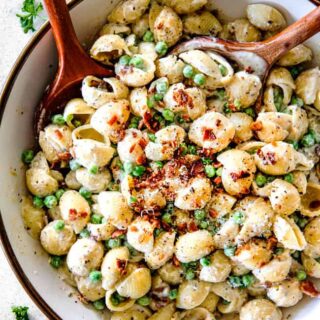 Creamy bacon and pea pasta salad in a bowl with two wooden serving spoons.
