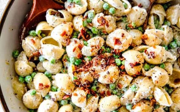 Creamy bacon and pea pasta salad in a bowl with two wooden serving spoons.
