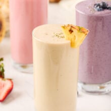 three different smoothies in glasses with pineapple smoothie in the front