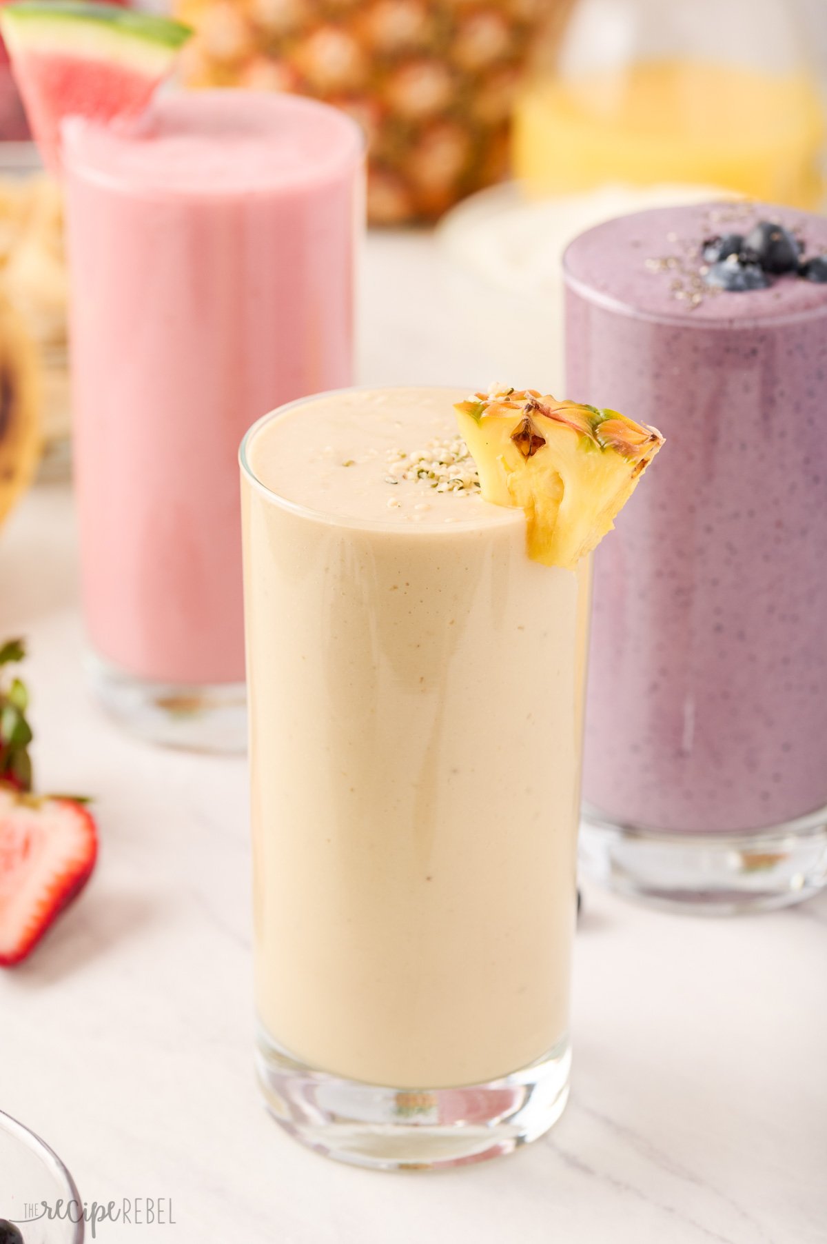 three different smoothies in glasses with pineapple smoothie in the front