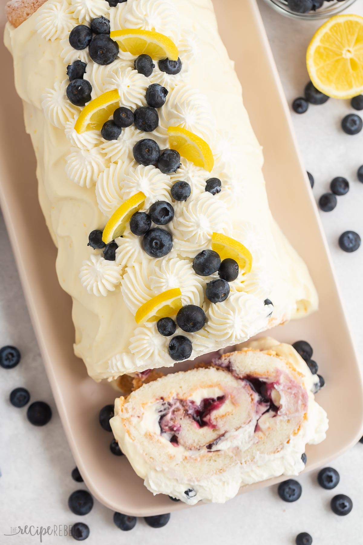 overhead image of lemon blueberry angel food cake roll on plate with one slice cut