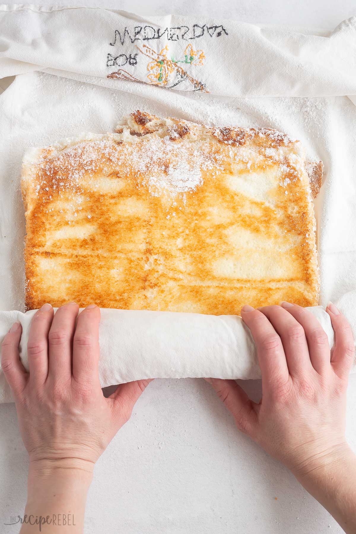 rolling up angel food cake in clean towel with powdered sugar