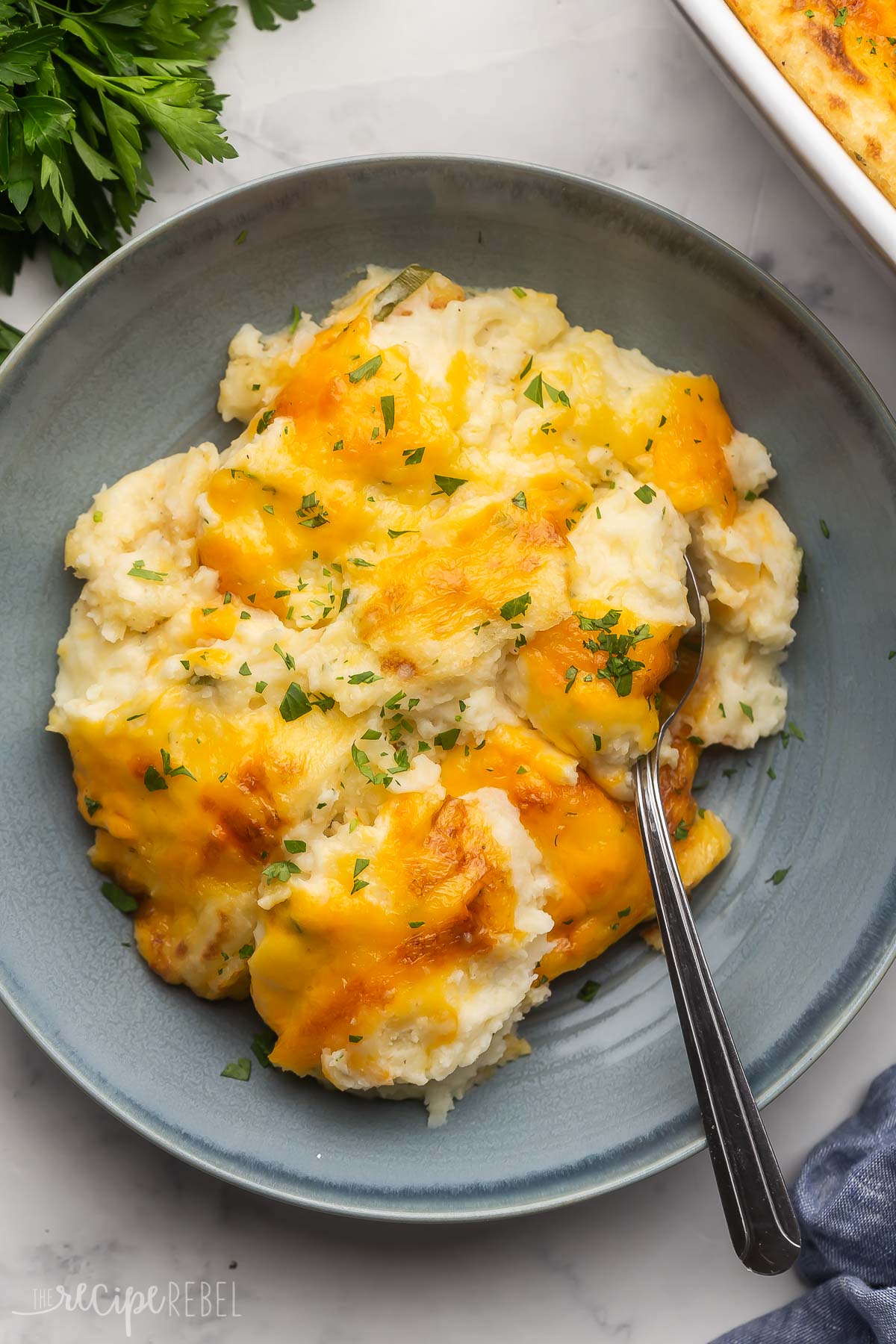 cheesy mashed potatoes on a blue plate with spoon stuck in.