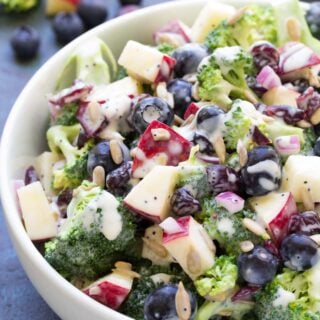 Broccoli salad topped with blueberries in a large white serving bowl.