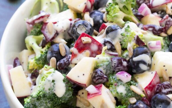 Broccoli salad topped with blueberries in a large white serving bowl.