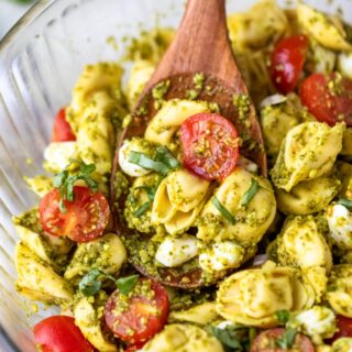 A bowl of pesto tortellini salad with a wooden spoon.