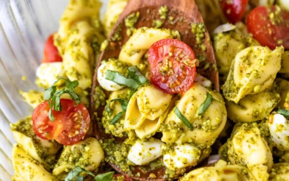 A bowl of pesto tortellini salad with a wooden spoon.