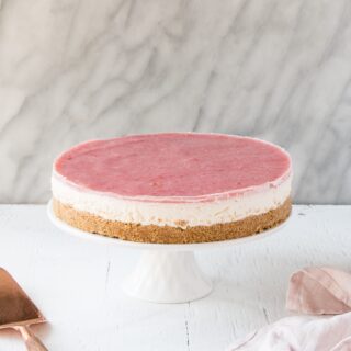 A whole no-bake rhubarb cheesecake on a white cake stand.