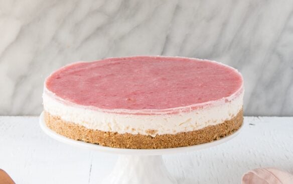 A whole no-bake rhubarb cheesecake on a white cake stand.