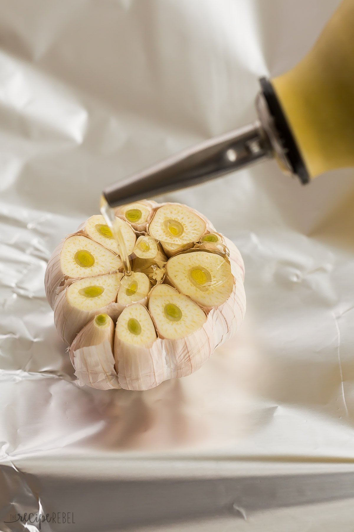 oil being drizzled on whole garlic head on tin foil