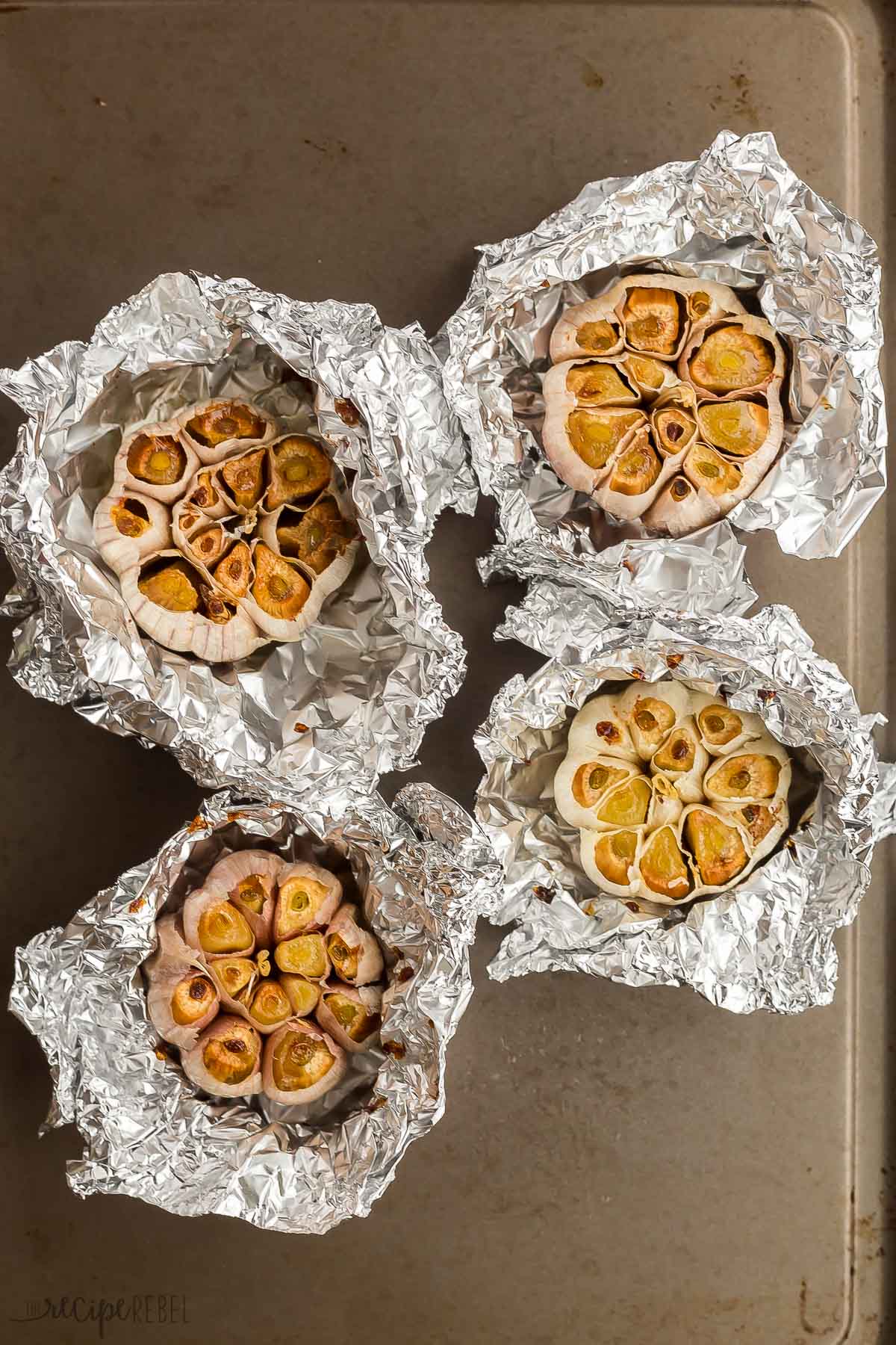 four roasted garlic heads sitting on tin foil