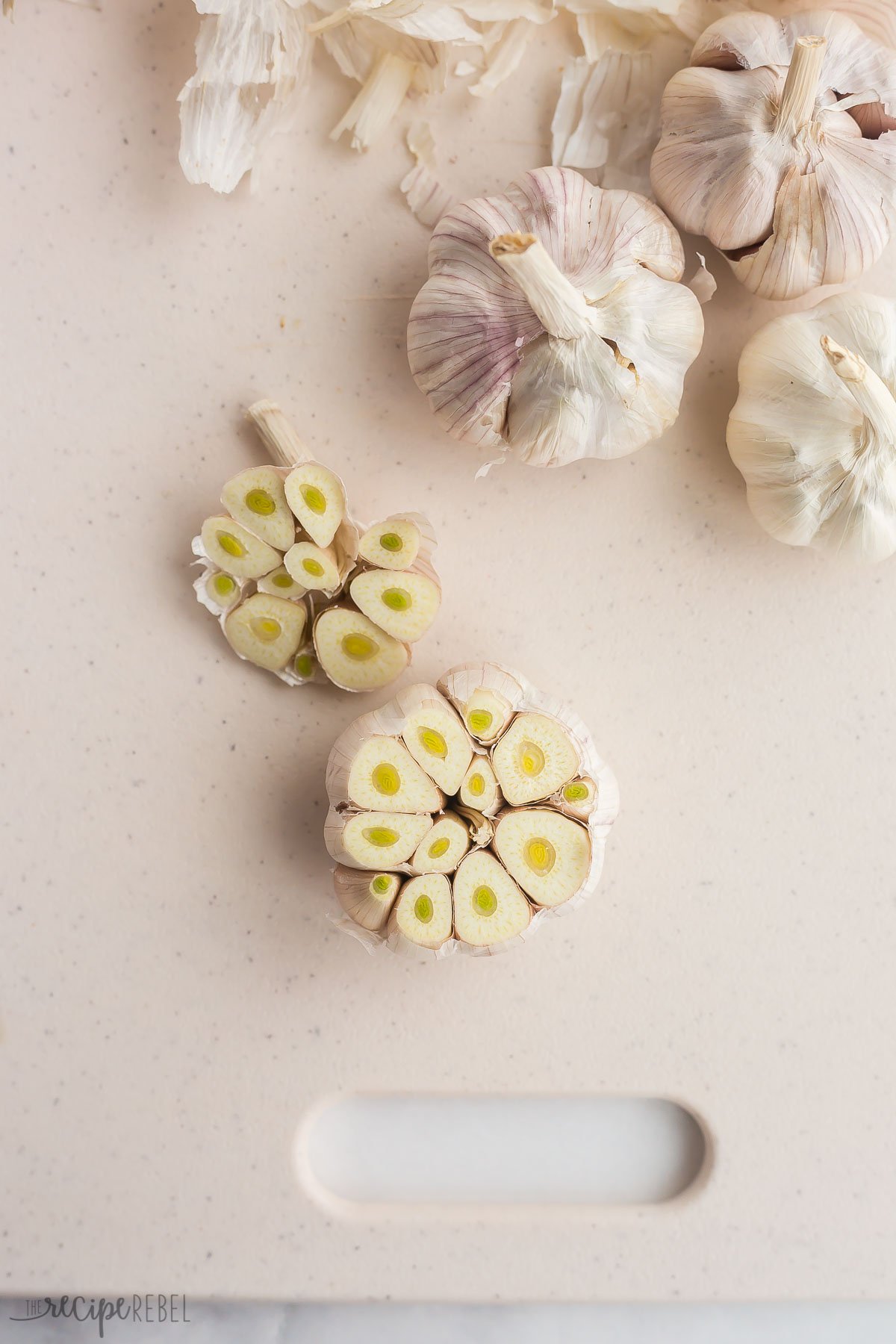 tops being cut off of garlic heads for roasting