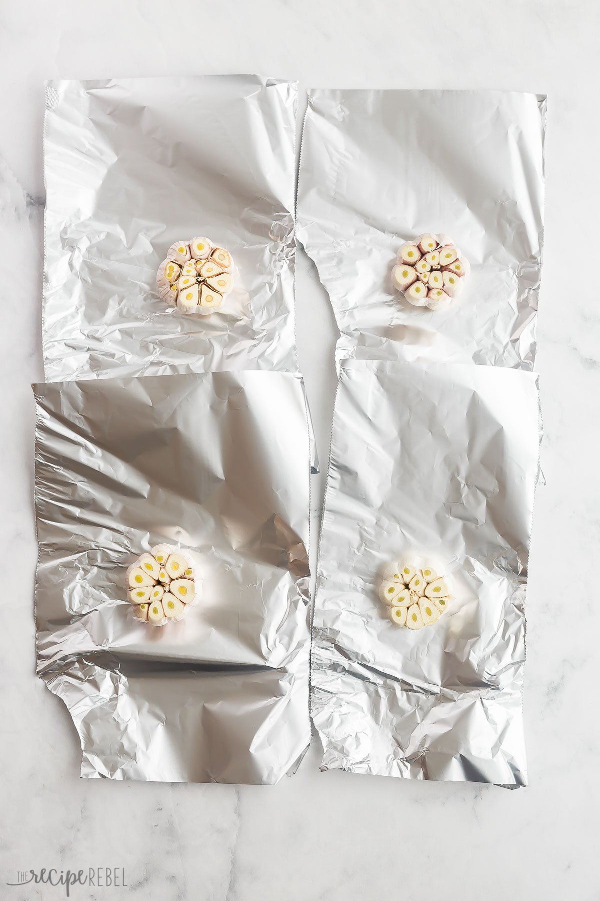 four garlic heads sitting on tin foil ready for roasting