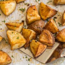 metal ladle scooping roasted red potatoes from baking sheet