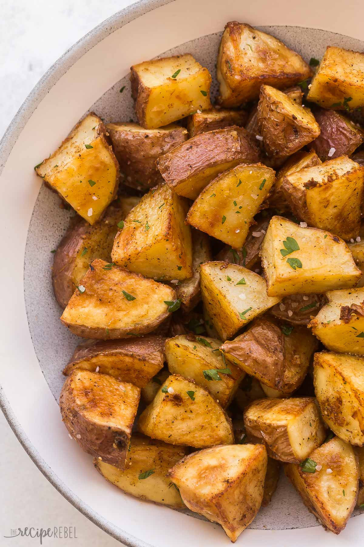close up image of roasted red potatoes in grey and white bowl