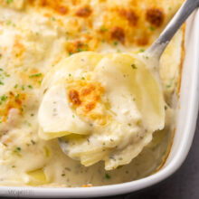 square image of a metal spoon scooping scalloped potatoes.