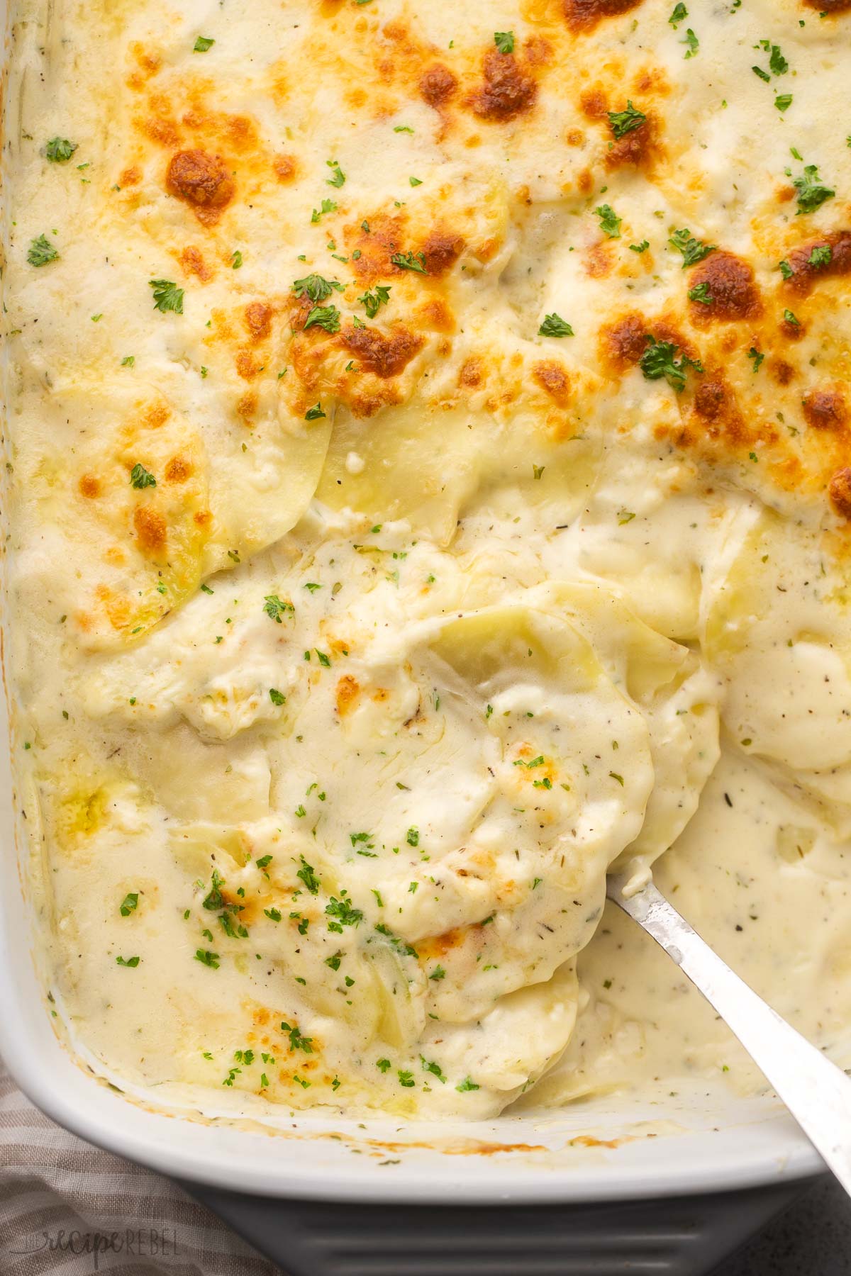 overhead image of spoon scooping cheesy scalloped potatoes out of dish.
