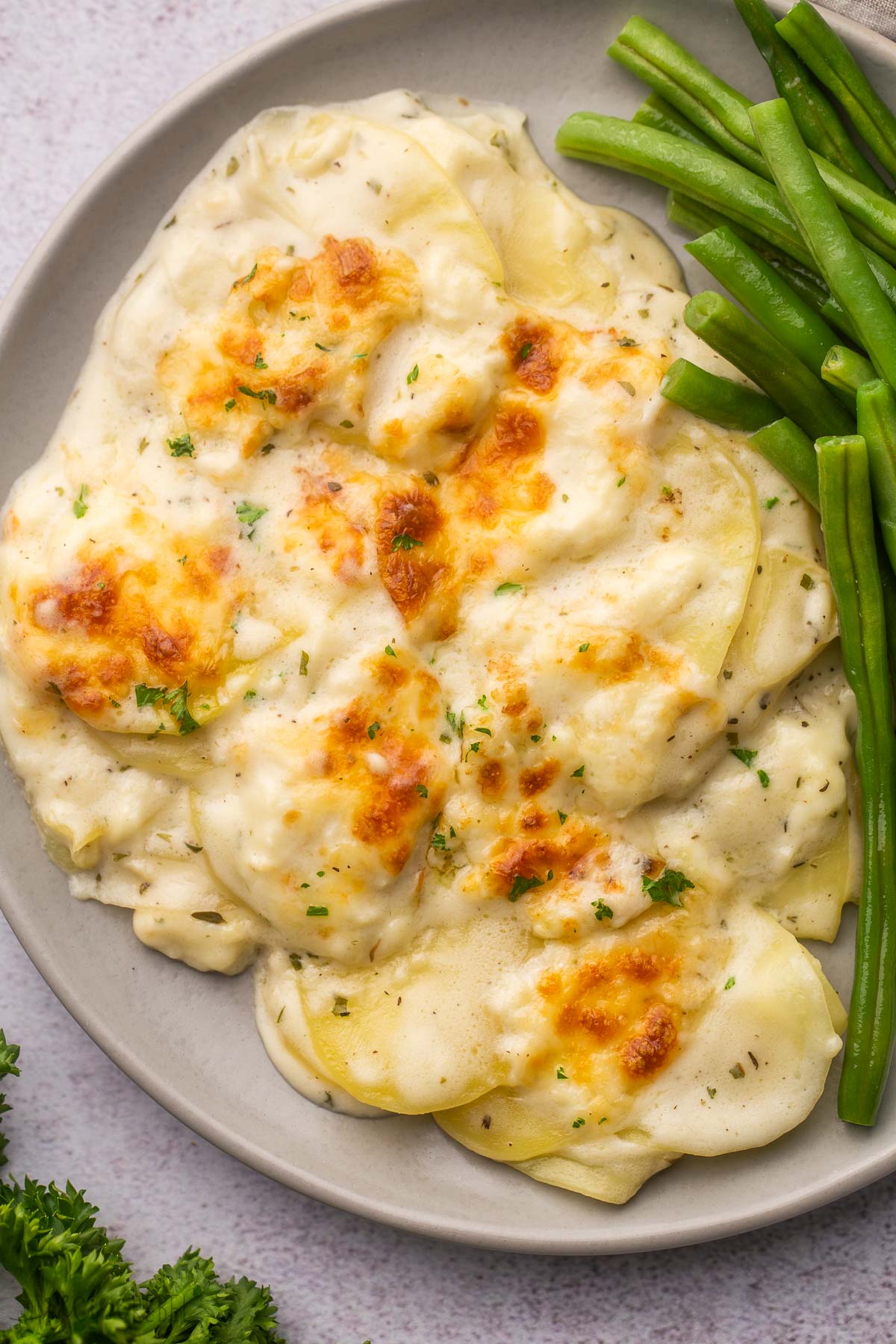 plate of cheesy scalloped potatoes with green beans on the side.