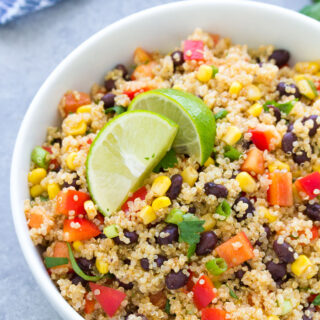 A large bowl of Southwest quinoa salad garnished with lime wedges.