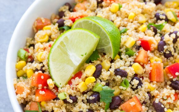 A large bowl of Southwest quinoa salad garnished with lime wedges.