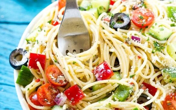 A fork twirls spaghetti from a bowl of spaghetti pasta salad.