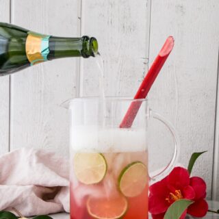 A glass of sparkling rhubarb margarita garnished with a stalk of rhubarb and limes.