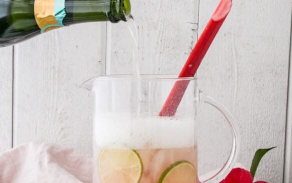 A glass of sparkling rhubarb margarita garnished with a stalk of rhubarb and limes.