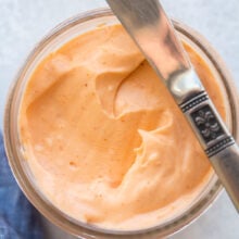 knife resting on the edge of a small jar of spicy mayo