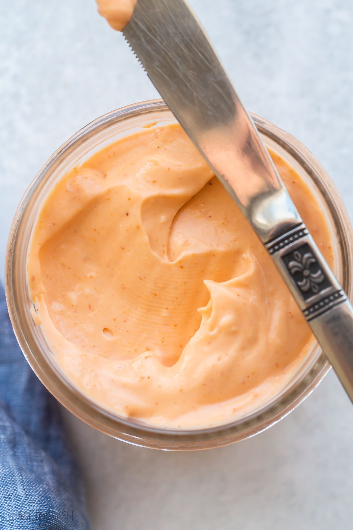 knife resting on the edge of a small jar of spicy mayo