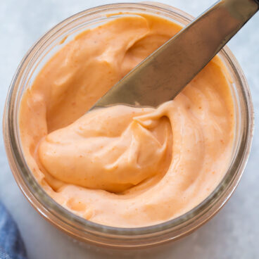 close up image of knife scooping spicy mayo from small jar