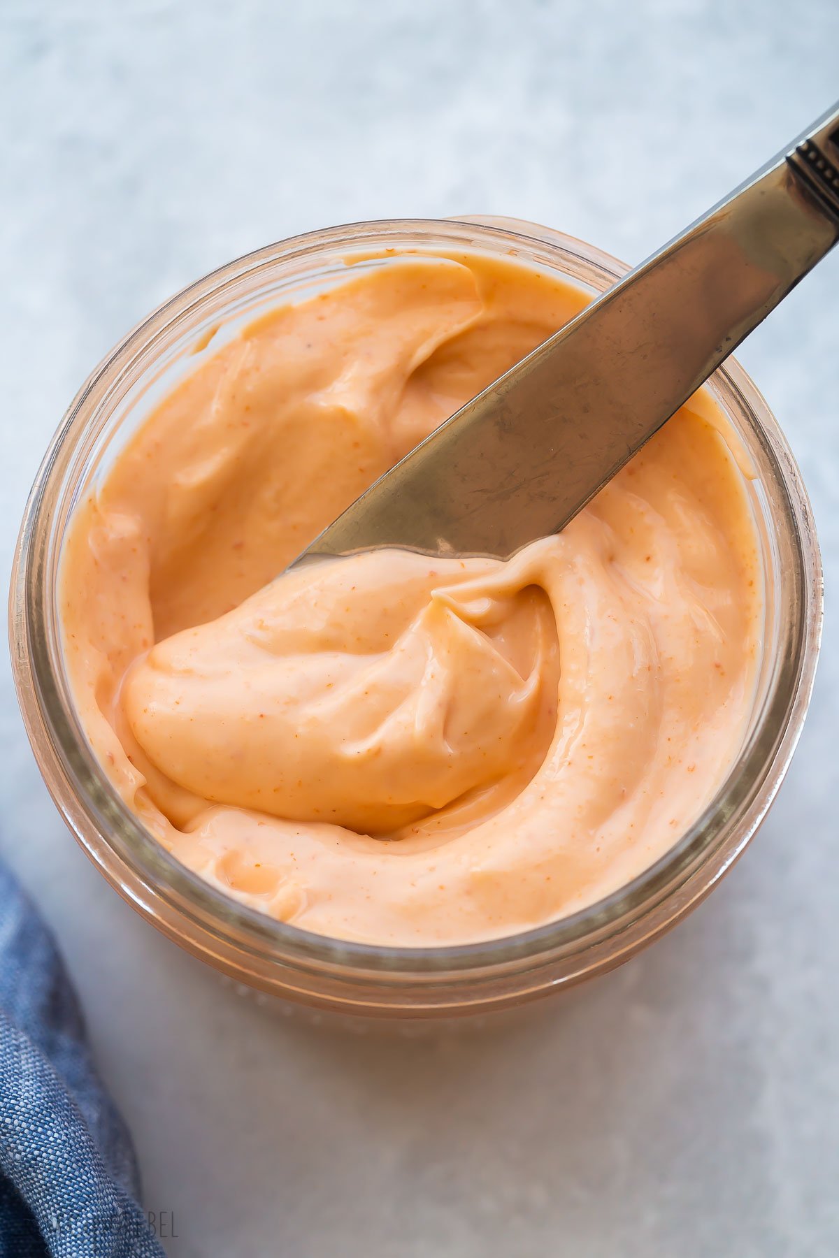 close up image of knife scooping spicy mayo from small jar