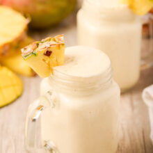 two tropical smoothies in glasses with fresh fruit in the background