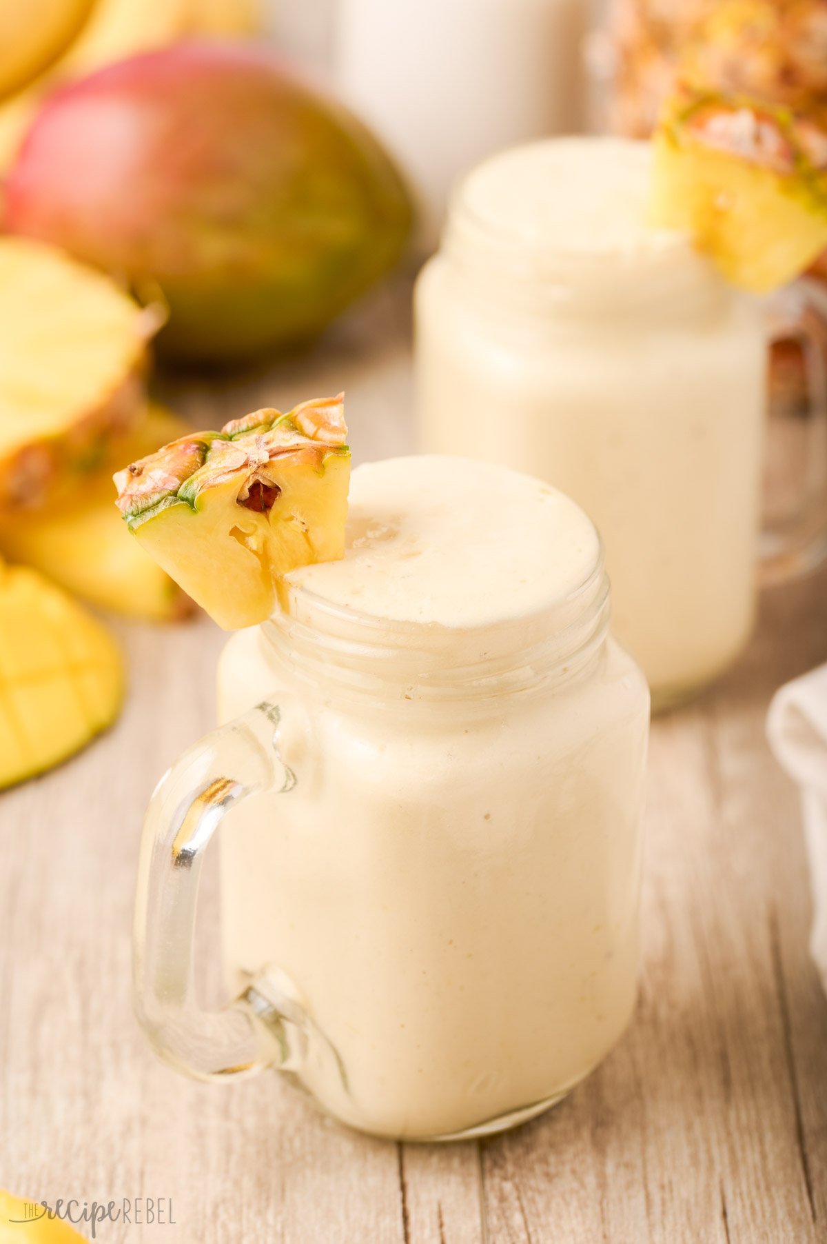 two tropical smoothies in glasses with fresh fruit in the background