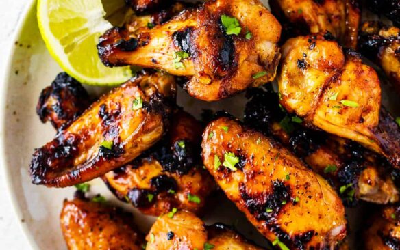 overhead of a pile of honey lice glazed thai chicken wings on a white plate garnished with lime