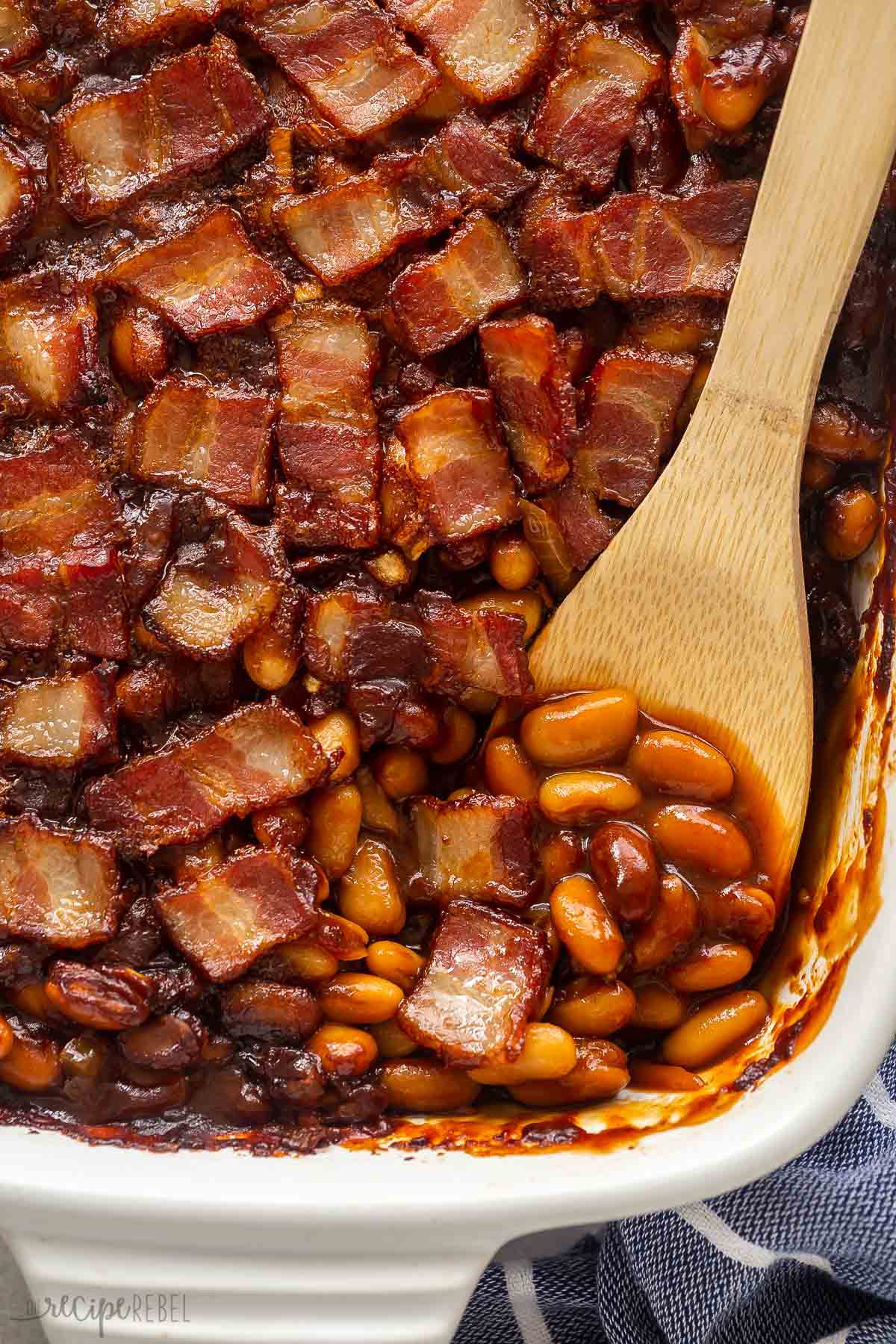 close up image of maple bacon baked beans with wooden spoon stuck in.