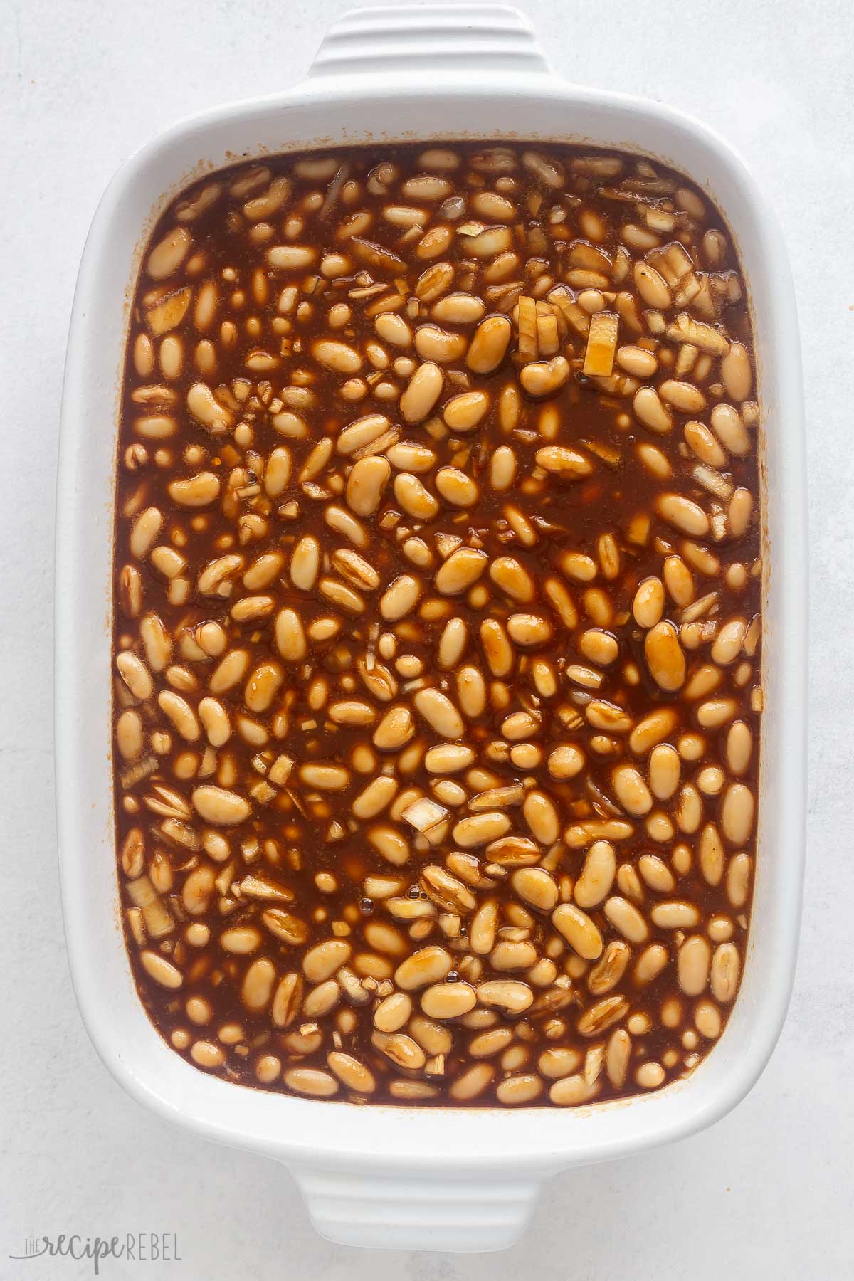 beans and sauce stirred together in white baking dish.