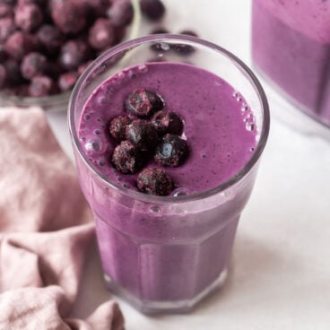 blueberry smoothie in tall glass with frozen blueberries on top