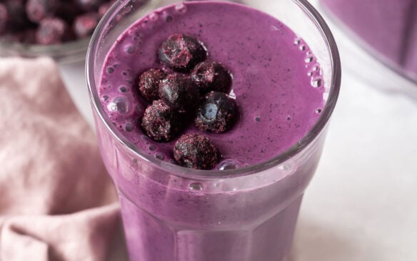 blueberry smoothie in tall glass with frozen blueberries on top