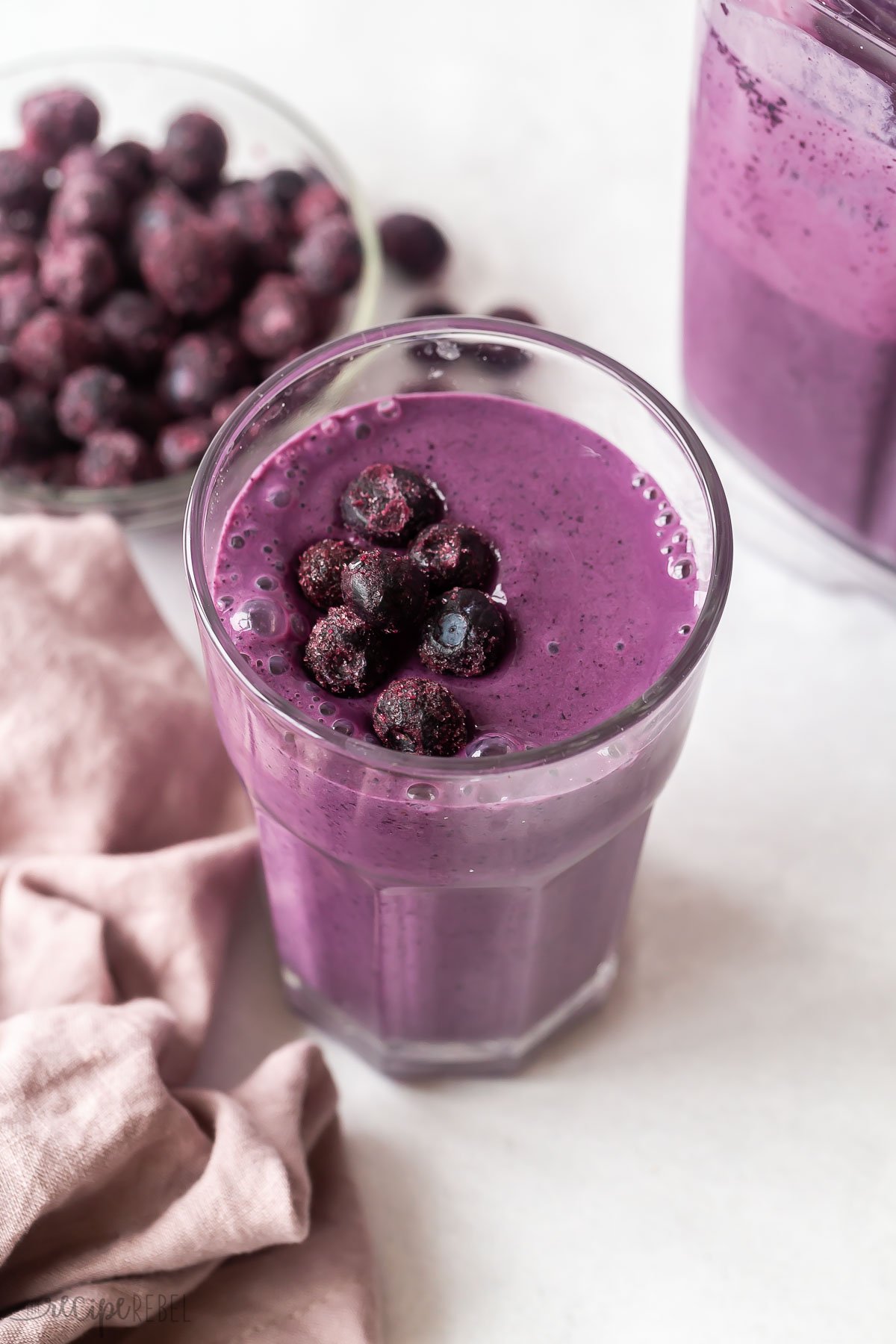blueberry smoothie in tall glass with frozen blueberries on top