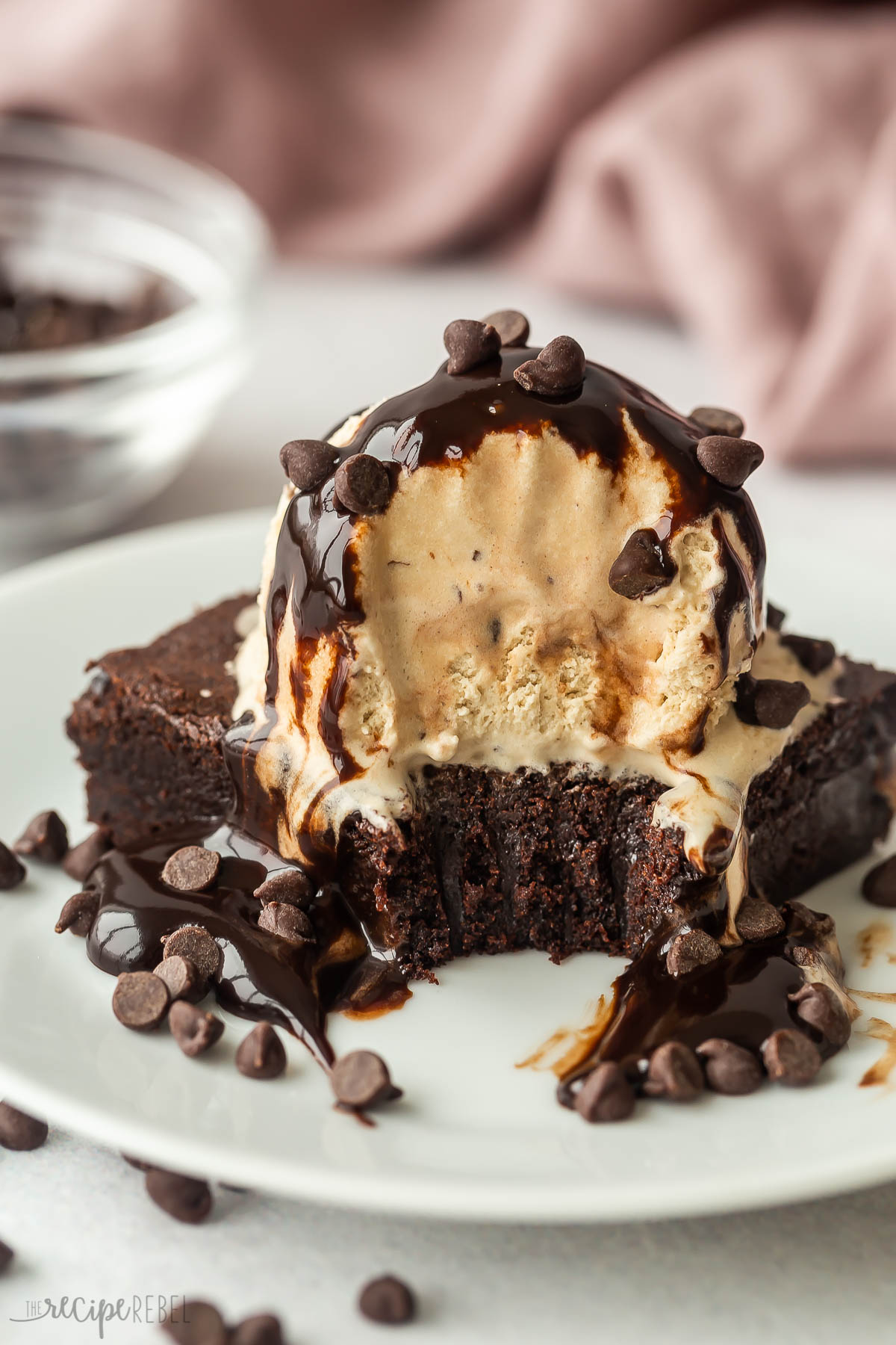 Brownie sundae on white plate with coffee ice cream chocolate sauce and mini chocolate chips.