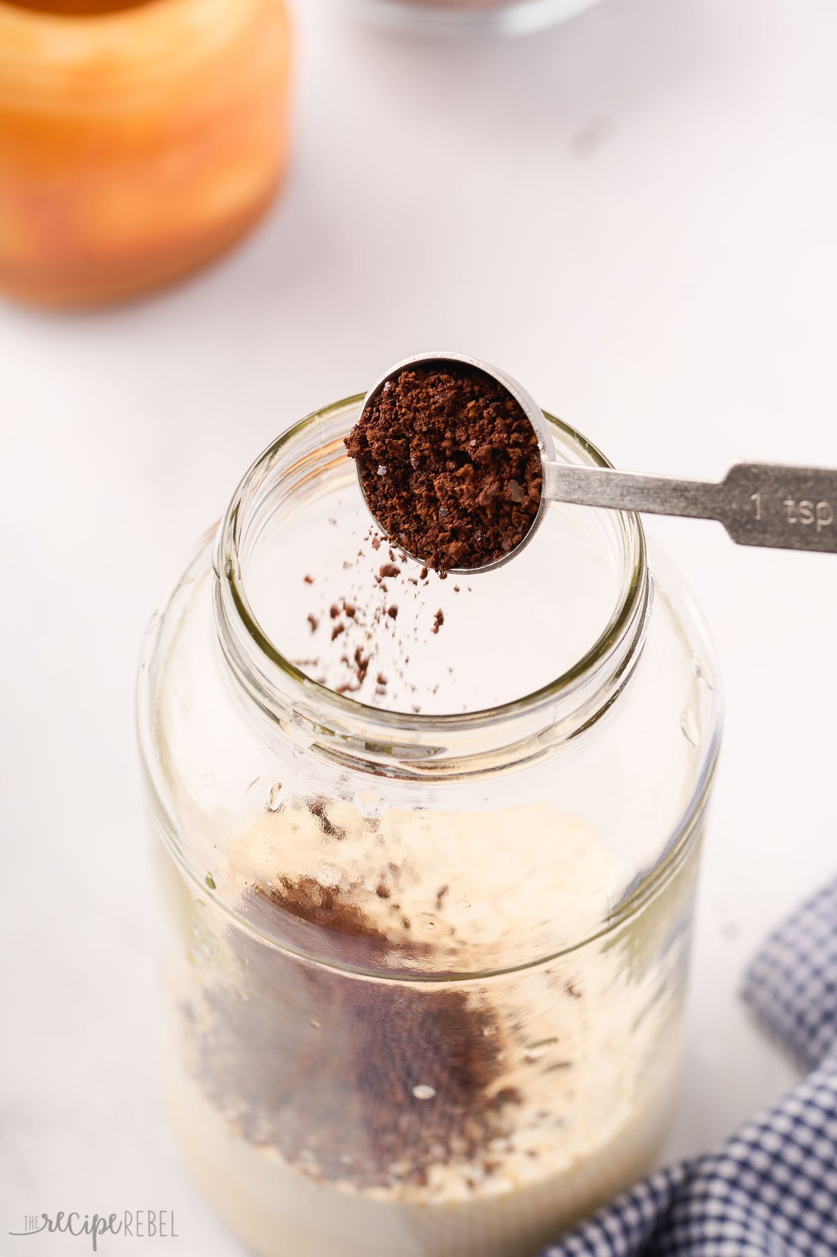 instant coffee being added to large glass jar.