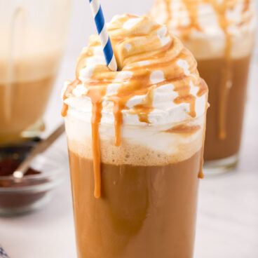 one caramel frappe in a glass with whipped cream caramel sauce and straw.