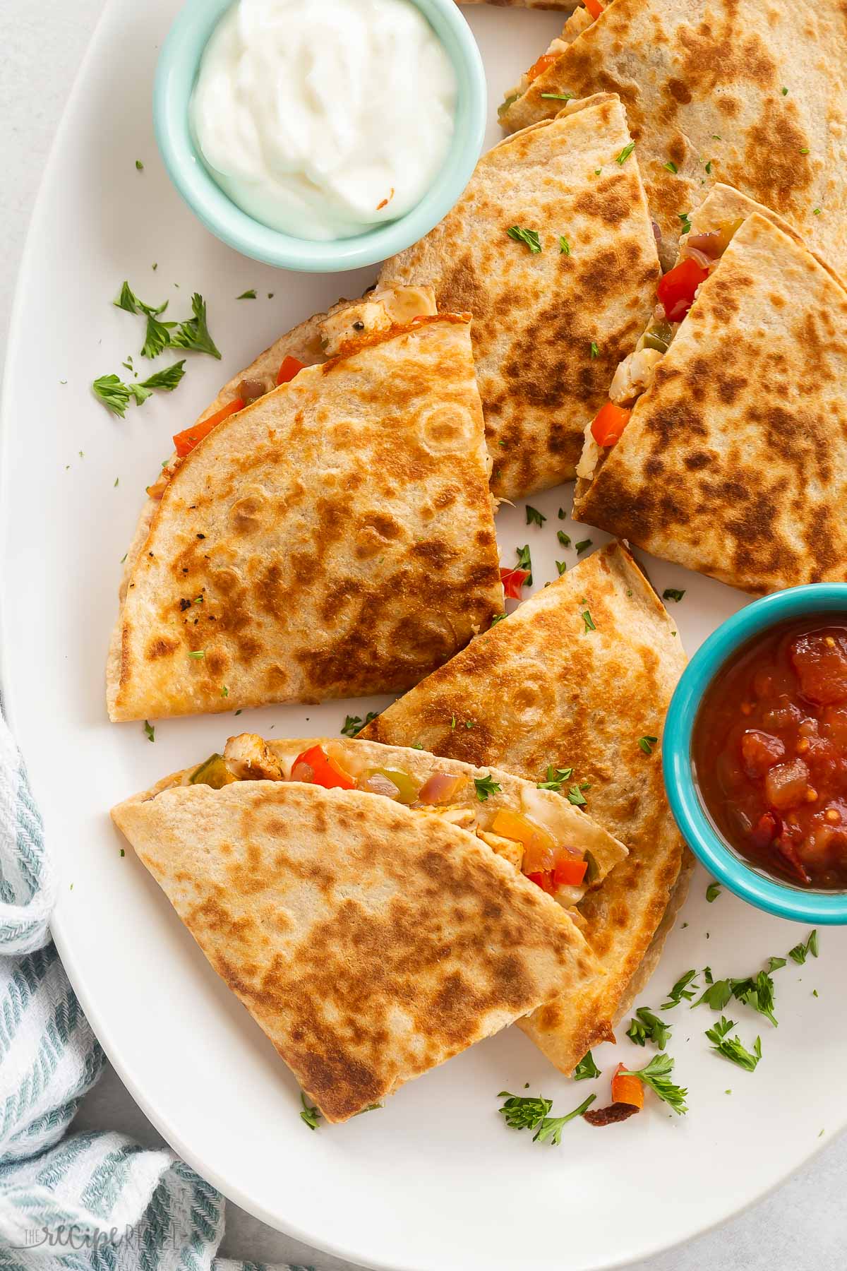 quartered chicken quesadillas on a white platter with salsa and sour cream.