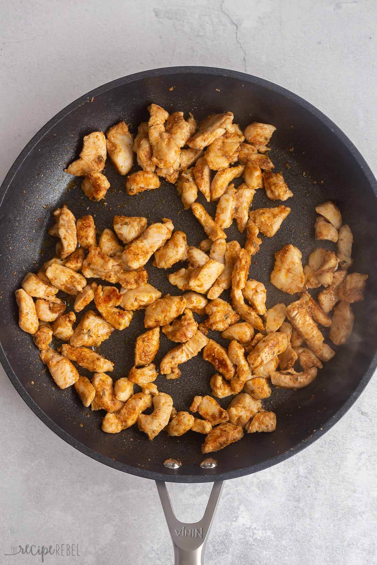 cooked chicken chunks with seasoning in a skillet.